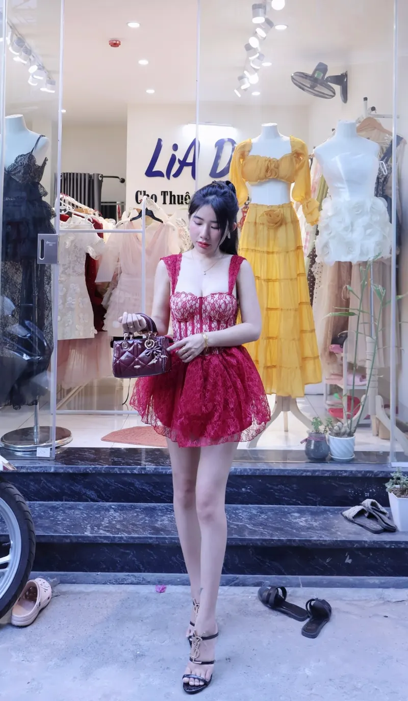 Nàng thơ trong đầm ren đỏ burgundy hai dây dáng xoè, cầm túi Lady mini trước showroom LiA Dress.